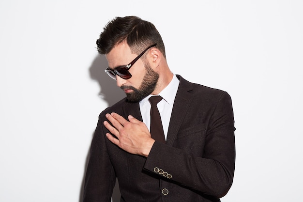 Hombre guapo con cabello negro y barba con camisa blanca, traje y gafas de sol en el fondo blanco del estudio, retrato.