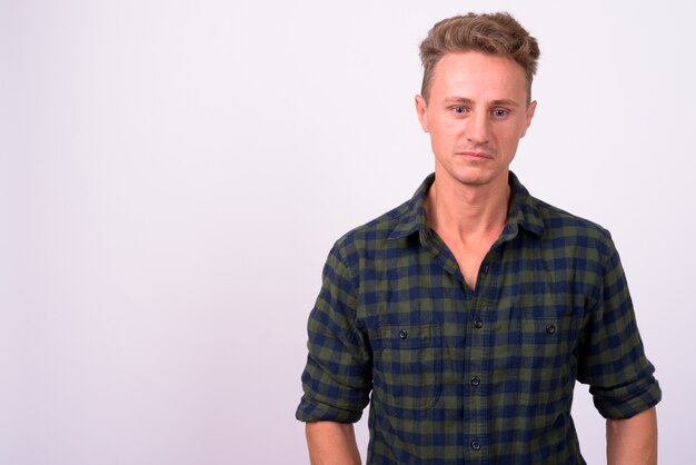 Hombre guapo con cabello rizado rubio vistiendo camisa a cuadros verde contra la pared blanca