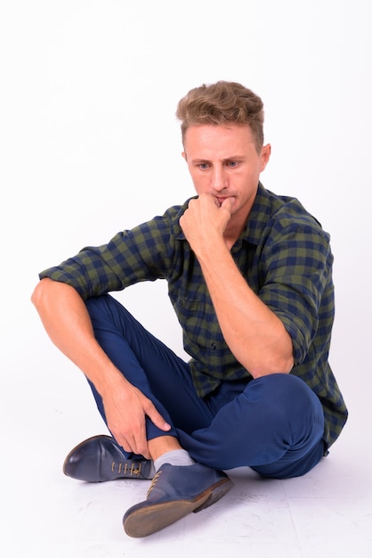 Hombre guapo con cabello rizado rubio vistiendo camisa a cuadros verde contra la pared blanca