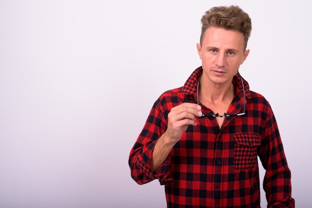 Hombre guapo con cabello rizado rubio vistiendo camisa roja a cuadros contra la pared blanca