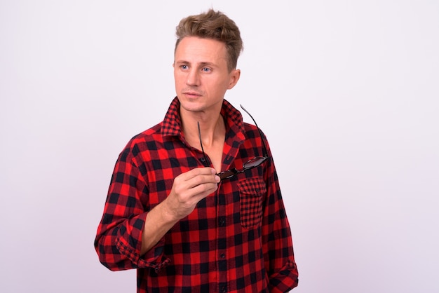 Hombre guapo con cabello rizado rubio vistiendo camisa roja a cuadros contra la pared blanca