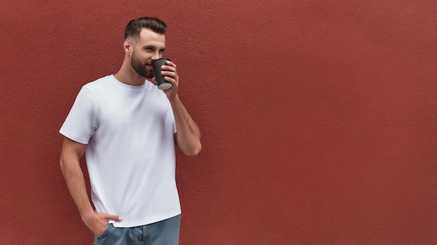 Hombre guapo de café recién hecho con ropa informal sosteniendo una taza de café y mirando a un lado mientras