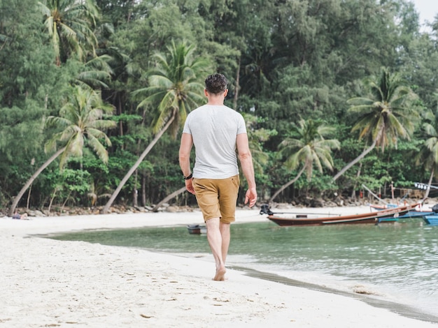 Foto hombre guapo caminando a lo largo de una impresionante playa de arena blanca