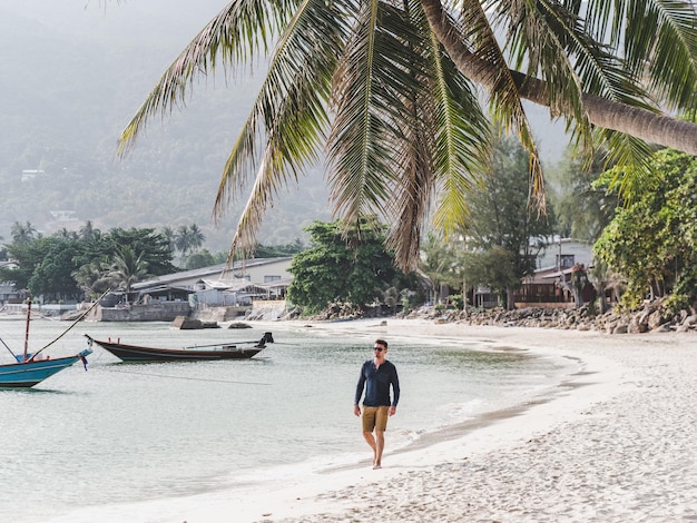 Foto hombre guapo caminando a lo largo de una impresionante playa de arena blanca