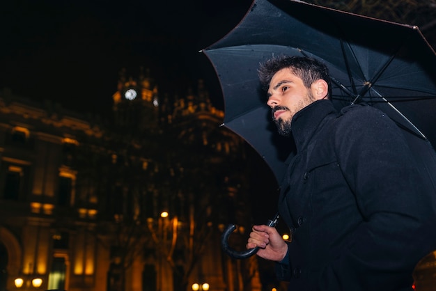 Hombre guapo caminando en Madrid por la noche bajo la lluvia.