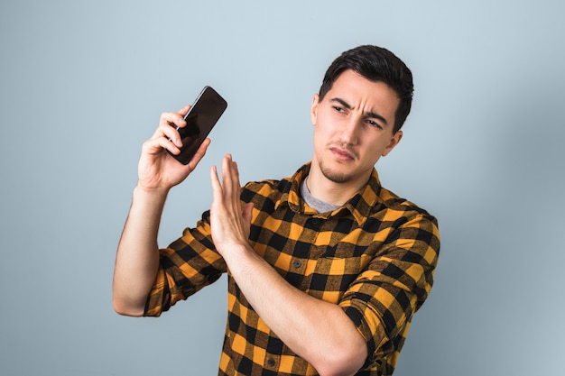 Hombre guapo con camisa amarilla molesto por la voz de alguien en el teléfono haciendo un gesto con la mano diciendo que no más