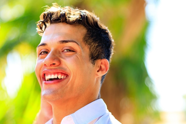 Hombre guapo con camisa blanca con una sonrisa blanca mirando a la cámara en el parque de verano