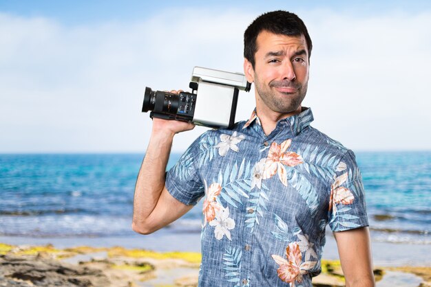 Hombre guapo con camisa de flor de filmación en la playa