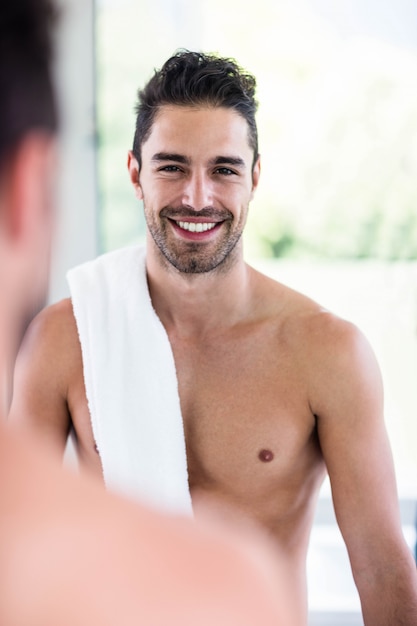 Hombre guapo sin camisa mirando en el espejo en el baño