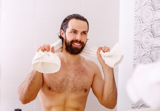 Hombre guapo sin camisa mirando en el espejo en el baño