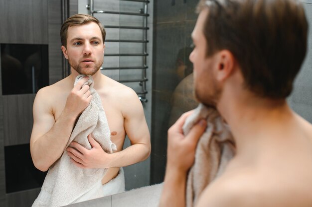 Hombre guapo sin camisa mirando en el espejo en el baño