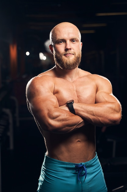 Hombre guapo sin camisa con músculos tonificados de pie con los brazos cruzados mientras mira a la cámara