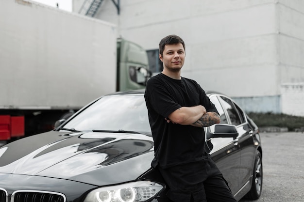 Un hombre guapo con una camiseta está de la mano cerca de un auto negro Comprando y alquilando un auto