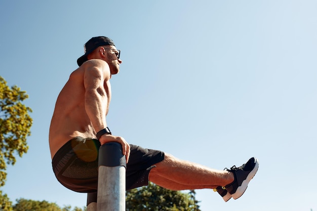 Hombre guapo en el campo deportivo El deportista el chico realiza ejercicios difíciles gimnasia deportiva Hombre musculoso haciendo ejercicio El concepto de un joven moderno