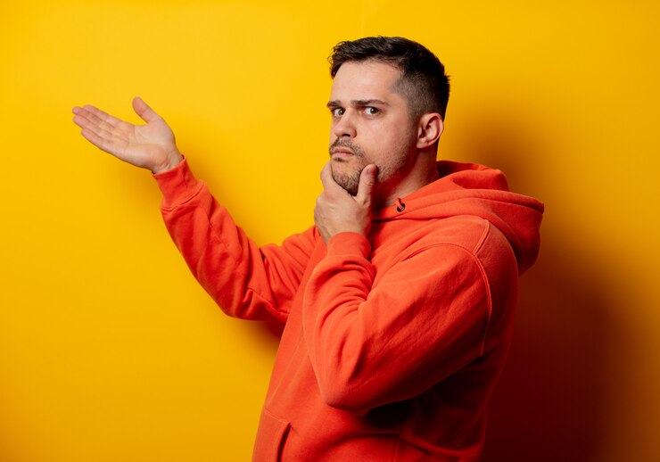 Foto hombre guapo con capucha en pared amarilla