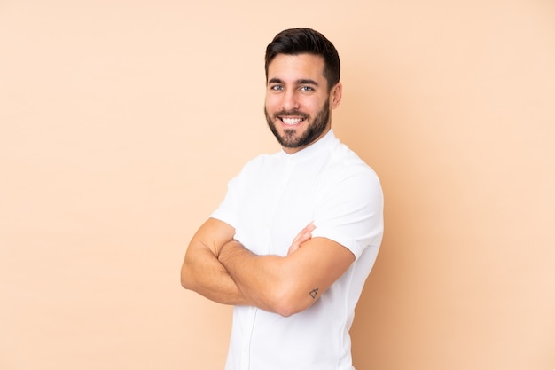 Hombre guapo caucásico aislado en la pared beige con los brazos cruzados y mirando hacia adelante