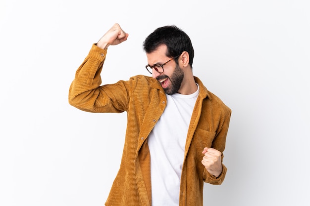 Hombre guapo caucásico con barba vistiendo una chaqueta de pana sobre pared blanca aislada celebrando una victoria