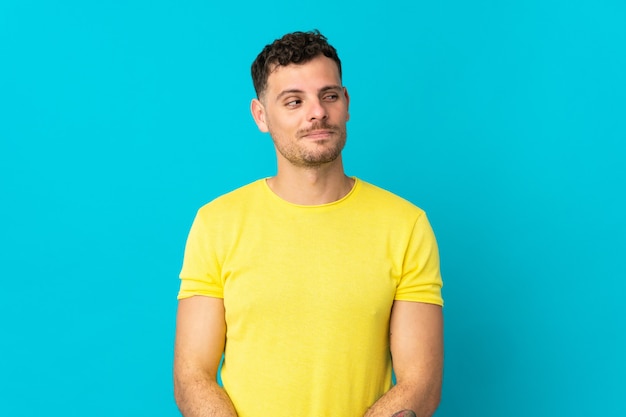 Hombre guapo caucásico joven aislado en azul haciendo gesto de dudas mirando de lado