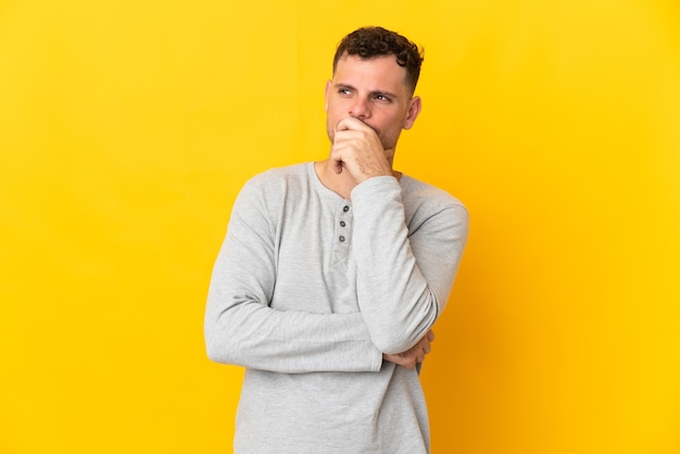 Hombre guapo caucásico joven aislado en la pared amarilla que tiene dudas y con expresión de la cara confusa