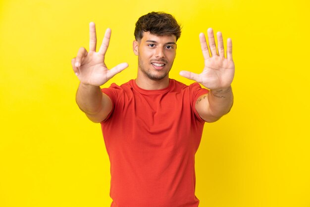 Hombre guapo caucásico joven aislado sobre fondo amarillo contando ocho con los dedos