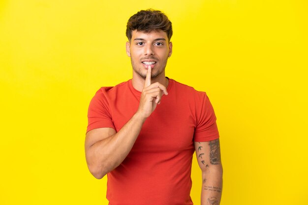 Hombre guapo caucásico joven aislado sobre fondo amarillo que muestra un signo de silencio gesto poniendo el dedo en la boca