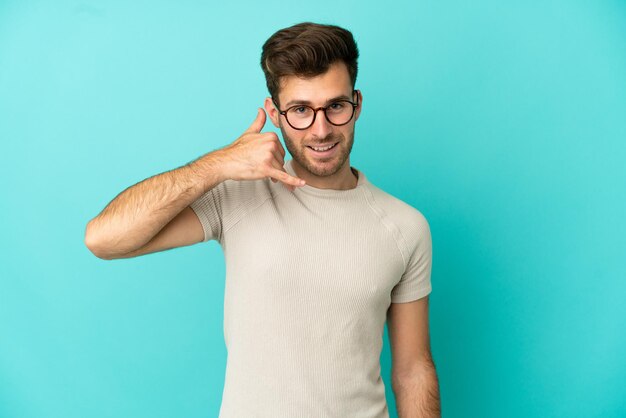 Hombre guapo caucásico joven aislado sobre fondo azul haciendo gesto de teléfono. Llámame señal