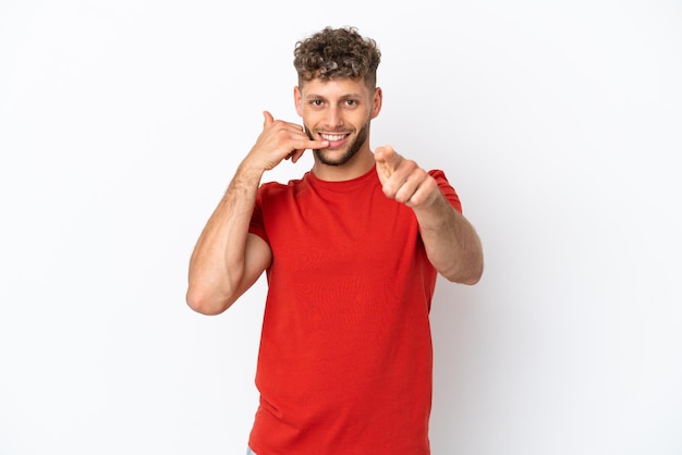 Hombre guapo caucásico joven aislado sobre fondo blanco haciendo gesto de teléfono y apuntando hacia el frente