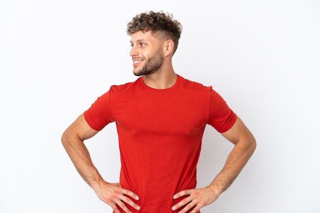 Hombre guapo caucásico joven aislado sobre fondo blanco posando con los brazos en la cadera y sonriendo