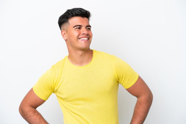 Hombre guapo caucásico joven aislado sobre fondo blanco posando con los brazos en la cadera y sonriendo