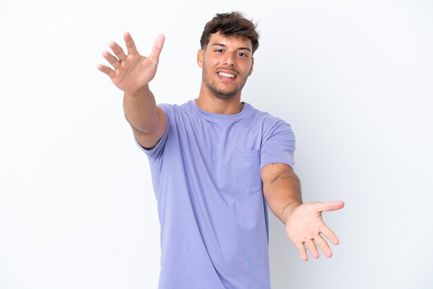 Hombre guapo caucásico joven aislado sobre fondo blanco que presenta e invita a venir con la mano