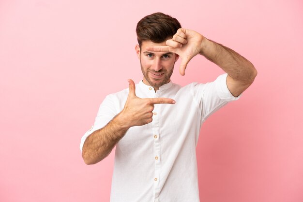 Hombre guapo caucásico joven aislado sobre fondo rosa enfocando la cara. Símbolo de encuadre