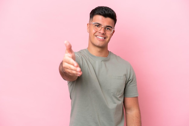 Hombre guapo caucásico joven aislado sobre fondo rosa estrecharme la mano para cerrar un buen trato