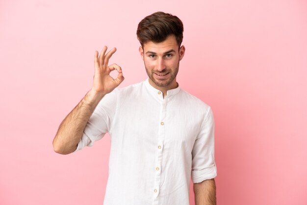 Hombre guapo caucásico joven aislado sobre fondo rosa mostrando signo ok con los dedos
