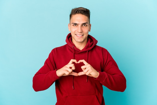 Foto hombre guapo caucásico joven aislado sonriendo y mostrando una forma de corazón con las manos.