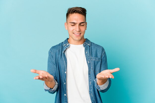 Hombre guapo caucásico joven aislado sosteniendo algo con las palmas, ofreciendo a la cámara.