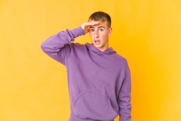 Hombre guapo caucásico joven mirando lejos manteniendo la mano en la frente.