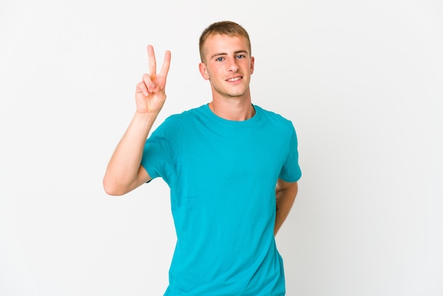 Hombre guapo caucásico joven que muestra el signo de la victoria y una amplia sonrisa.