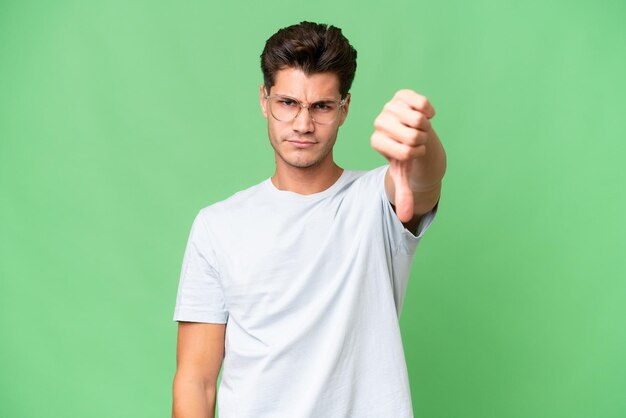 Hombre guapo caucásico joven sobre un fondo aislado que muestra el pulgar hacia abajo con expresión negativa