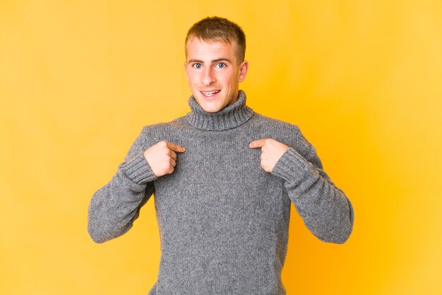 Hombre guapo caucásico joven sorprendido señalando con el dedo, sonriendo ampliamente.