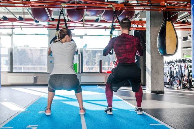 Hombre guapo caucásico y mujer joven se unen a la lección trx del club deportivo que se ejercita en el gimnasio joven pareja musculosa concentrada haciendo ejercicios de resistencia corporal total en interiores. Foto horizontal