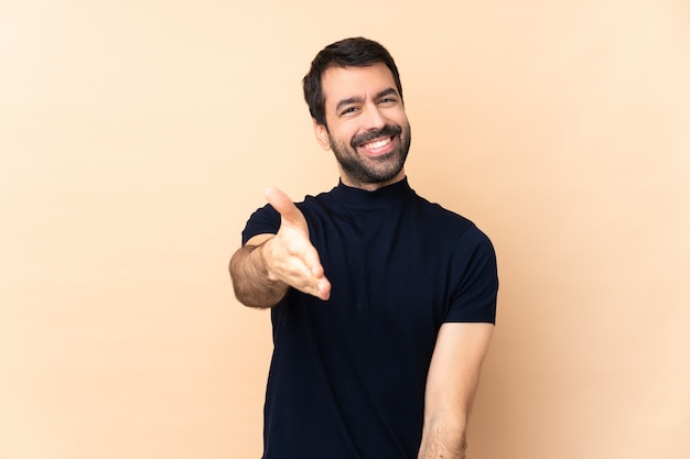 Hombre guapo caucásico sobre pared aislada estrechándole la mano para cerrar un buen negocio