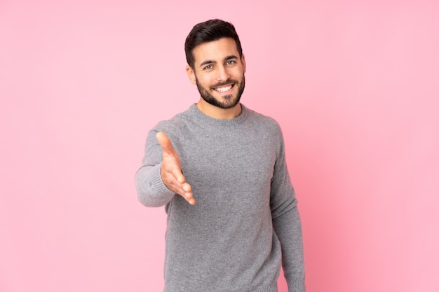 Hombre guapo caucásico sobre pared estrechándole la mano para cerrar un buen trato