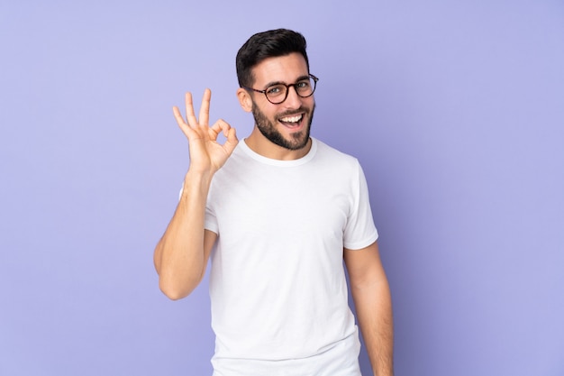 Hombre guapo caucásico sobre pared mostrando signo bien con los dedos