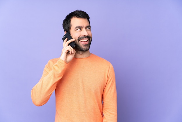 Hombre guapo caucásico sobre pared púrpura aislada manteniendo una conversación con el teléfono móvil