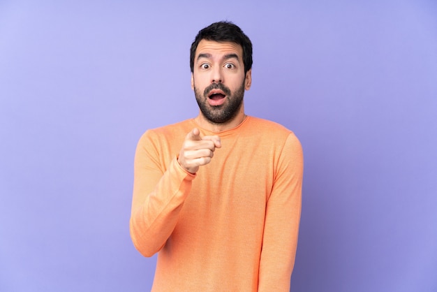 Hombre guapo caucásico sobre púrpura aislado sorprendido y apuntando al frente