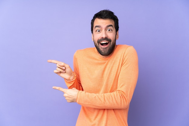 Hombre guapo caucásico sobre púrpura aislado sorprendido y apuntando hacia el lado