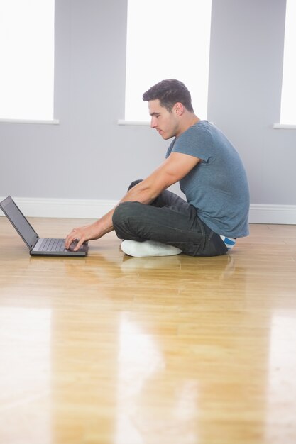 Hombre guapo centrado usando laptop sentado en el piso