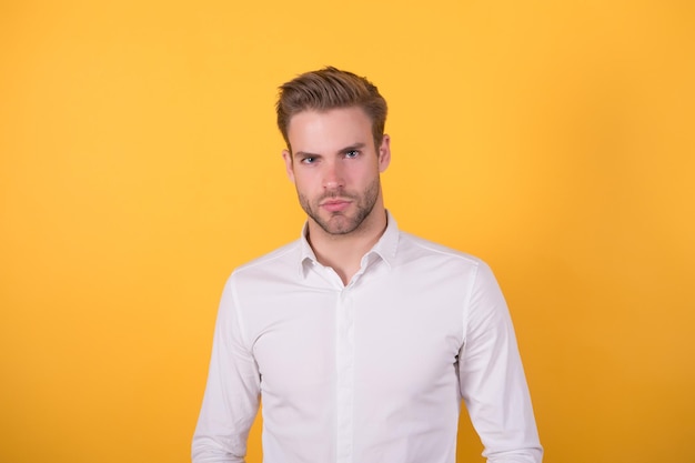 Hombre guapo con cerdas con camisa blanca de pie en la moda de negocios de fondo naranja