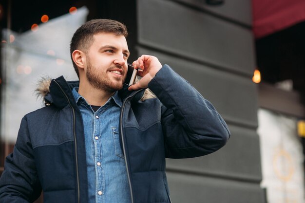 Hombre guapo con una chaqueta utiliza un teléfono de pie en la calle