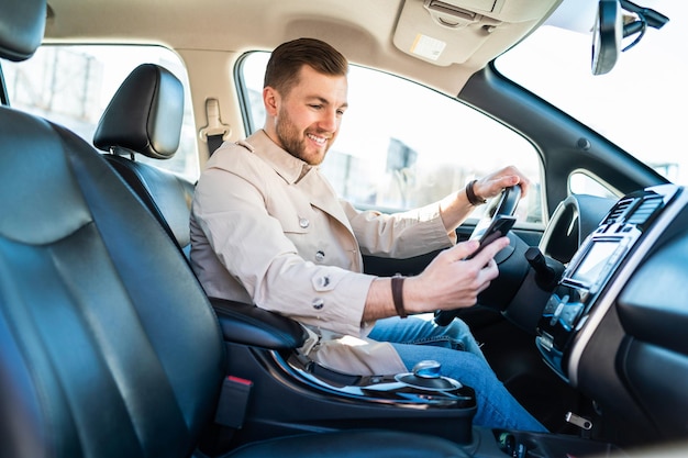 Hombre guapo en coche mira en smartphone